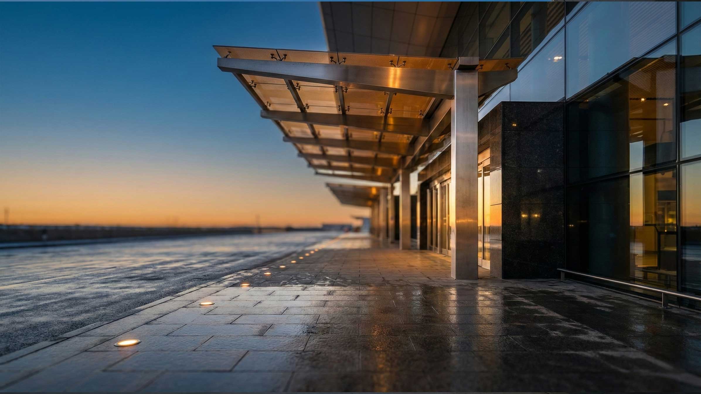 Airport terminal canopy beside an open apron at sunset.